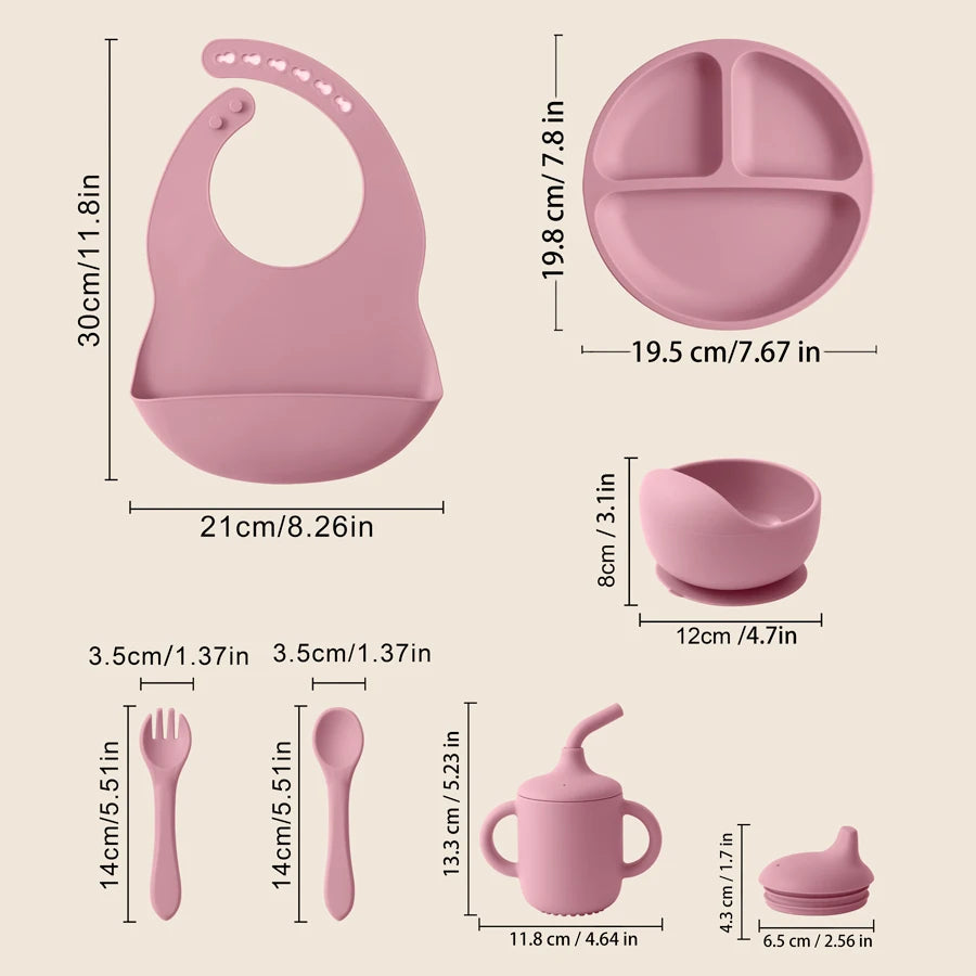 Pink baby feeding set with dimensions shown on a light beige background, including a silicone bib, three-compartment plate, bowl, sippy cup, spoon, and fork.