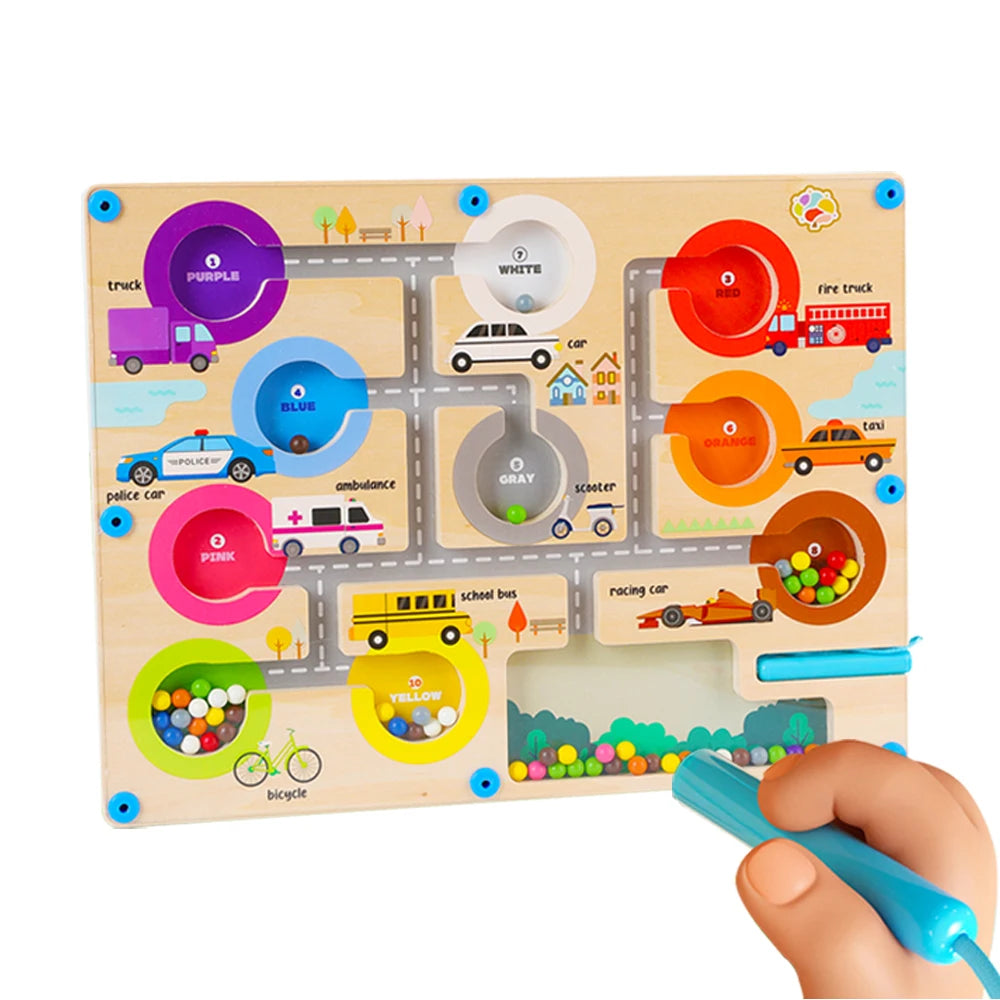 Colorful wooden toy road map with various vehicles and a hand holding a blue marker.