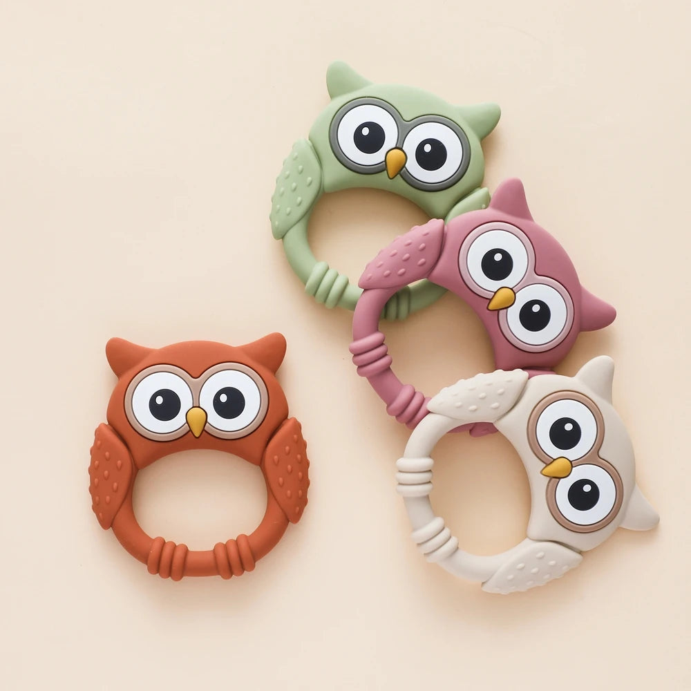 Four owl-shaped teething rings in different colors on a beige background