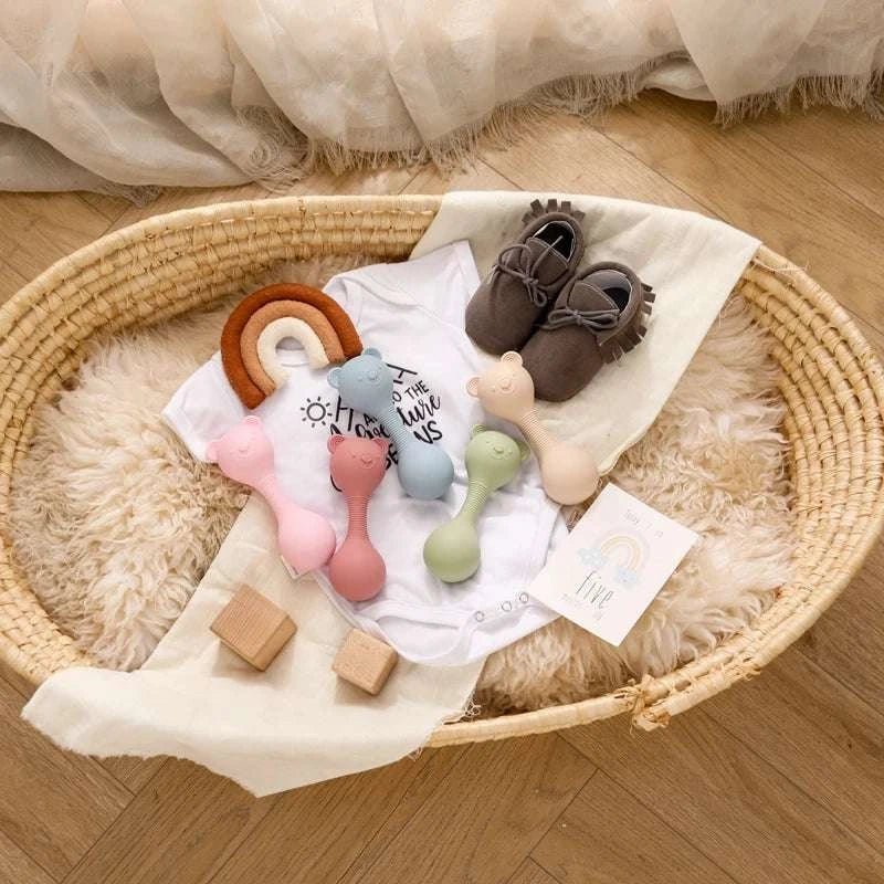 Baby Bear Silicone Teether Toy in a basket with toys and shoes, designed to soothe teething babies with its gentle silicone and engaging maracas feature.