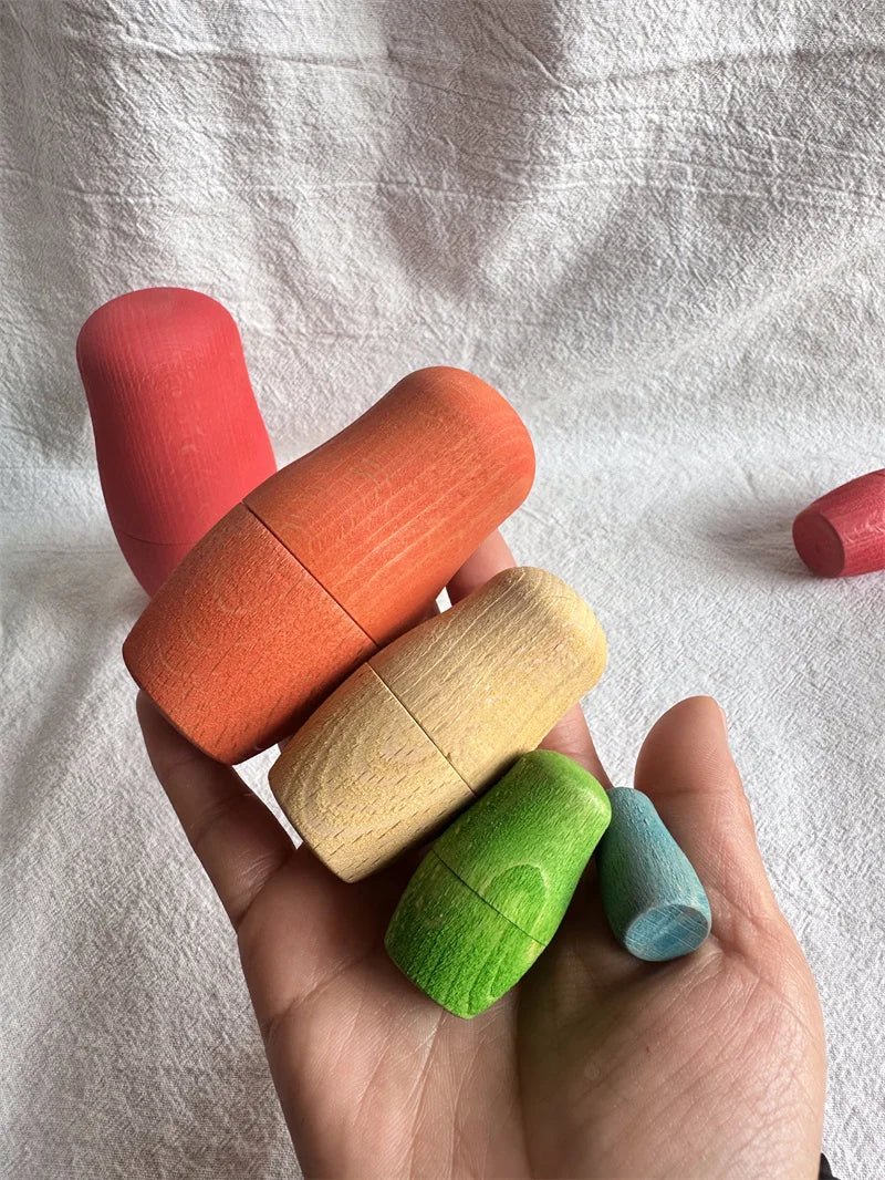 Montessori Beech Wood Rainbow Stacking Dolls: Hand holding natural beech wood nesting dolls, ideal for size exploration and fine motor skill development in Montessori play.
