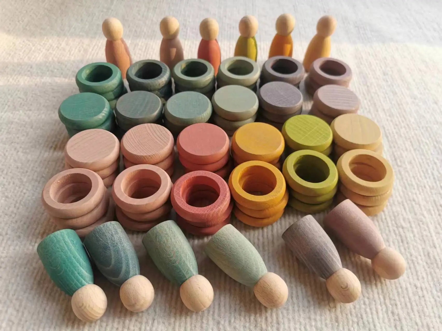Montessori Rainbow Stacking Coins and Rings with Peg Dolls, featuring beech wood figures and stackable elements, promotes fine motor skills and imaginative play.