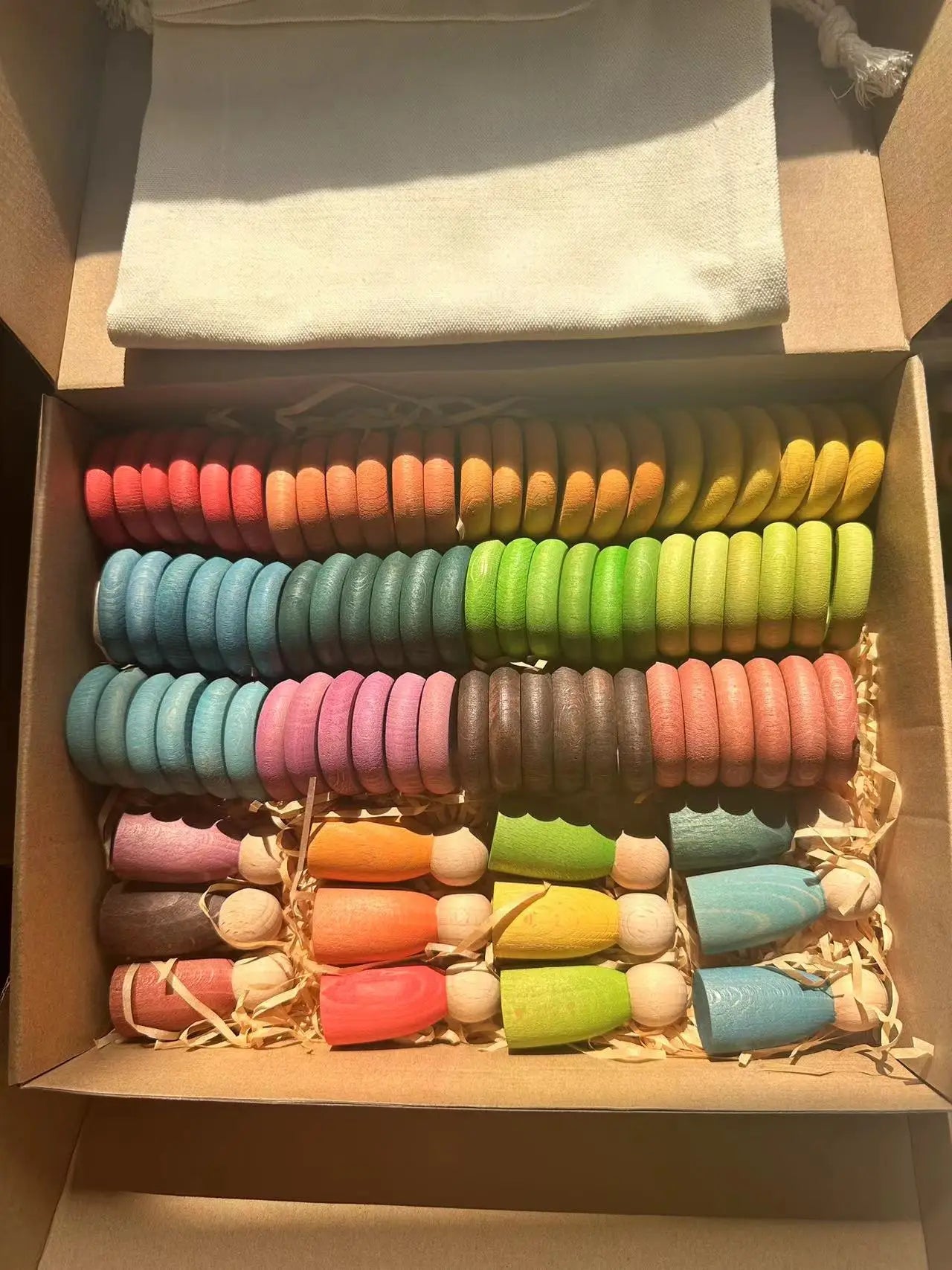 Montessori Rainbow Stacking Coins and Rings with Peg Dolls in a box, showcasing colorful, wooden elements designed for fine motor skill development and imaginative play.