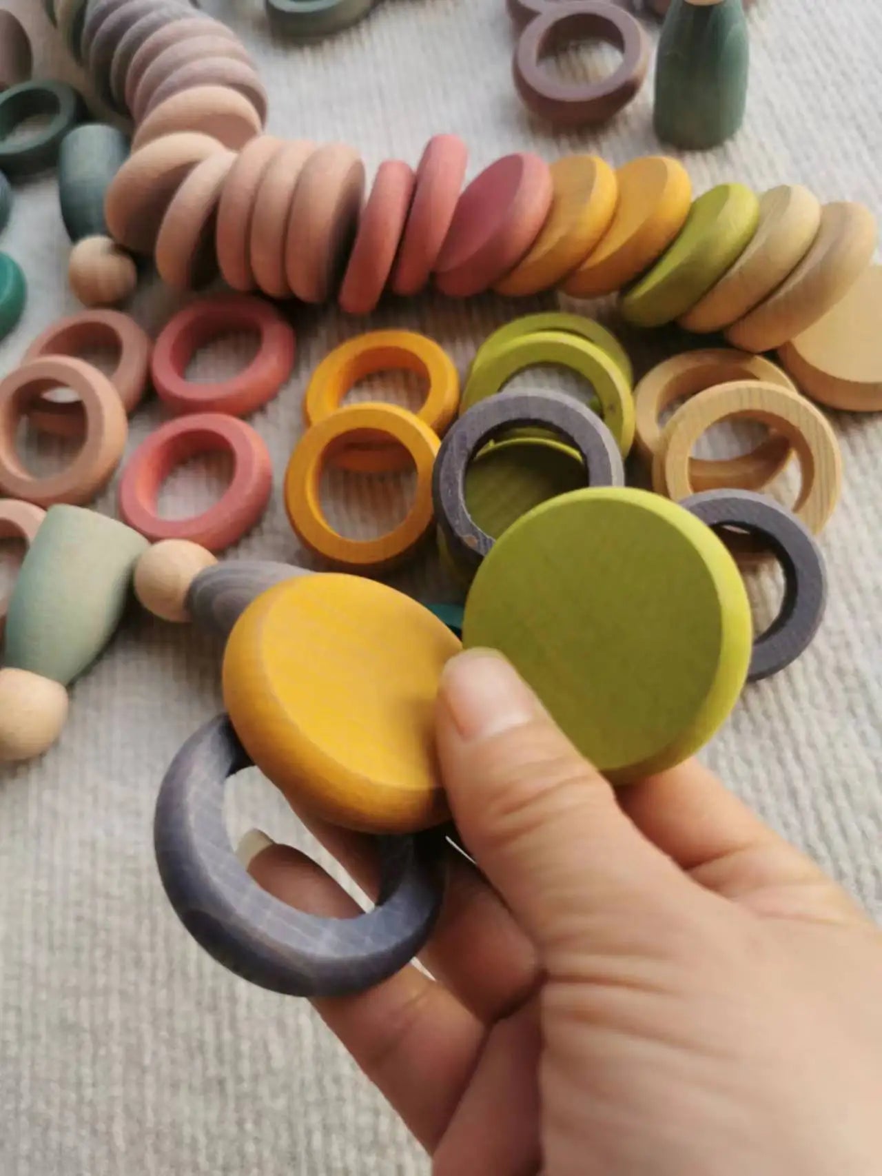 Hand holding Montessori Rainbow Stacking Coins and Rings with Peg Dolls, a wooden toy set designed for enhancing fine motor skills and imaginative play.
