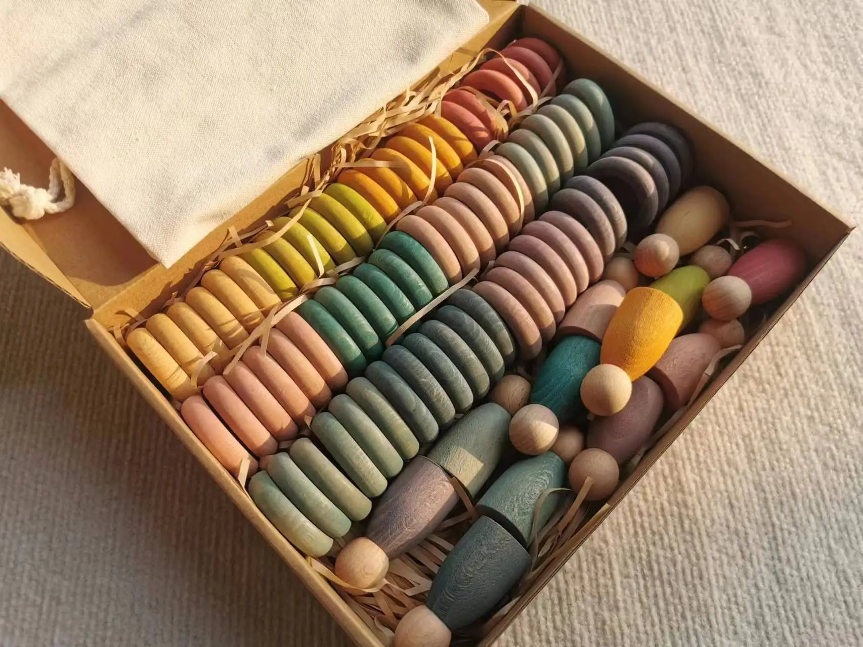 Montessori Rainbow Stacking Coins and Rings with Peg Dolls by Bajo in a box, showcasing wooden toys designed for developing fine motor skills and coordination in children.