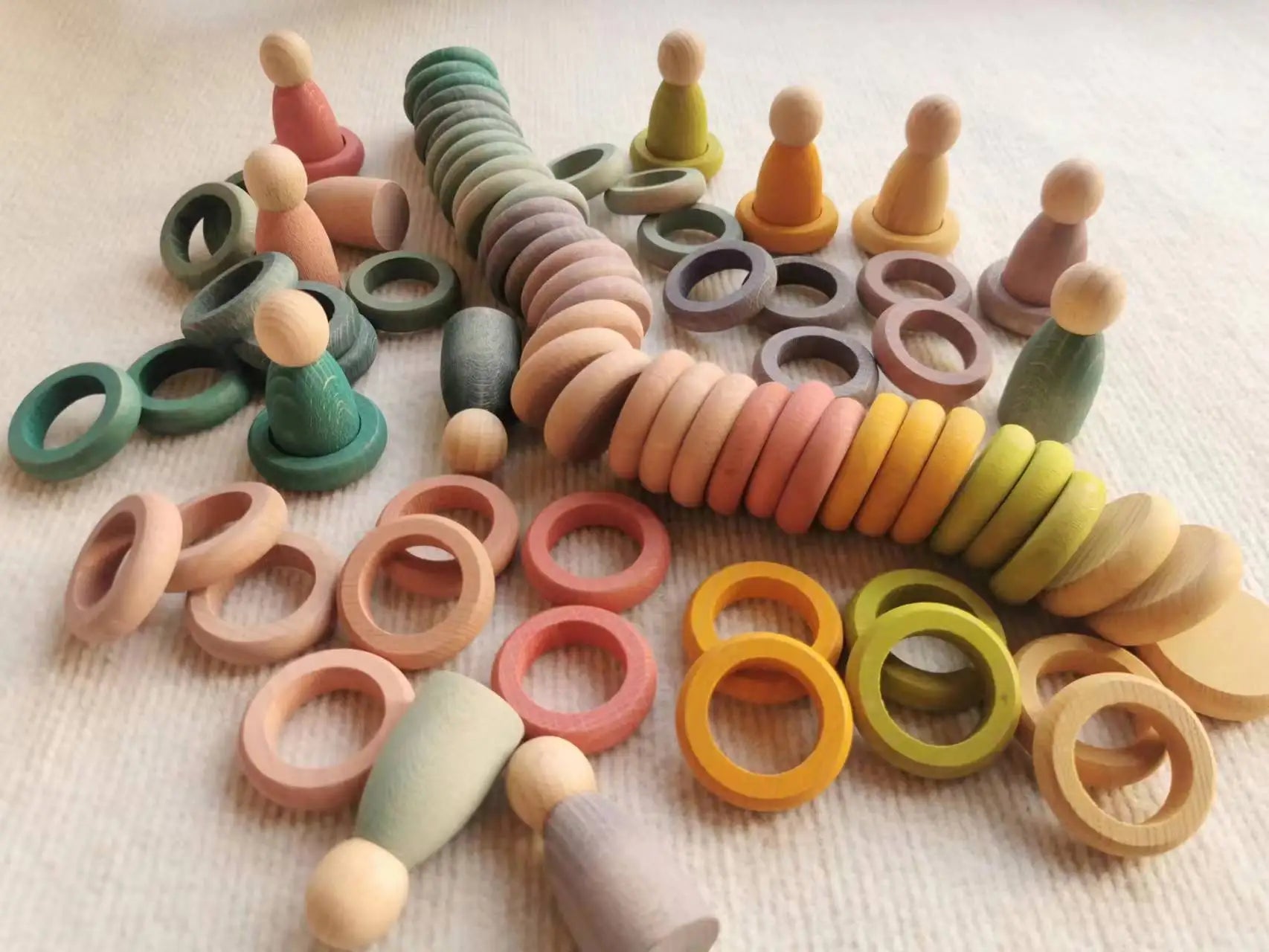 Montessori Rainbow Stacking Coins and Rings with Peg Dolls, a wooden toy set for enhancing fine motor skills and imaginative play, displayed in a group arrangement.